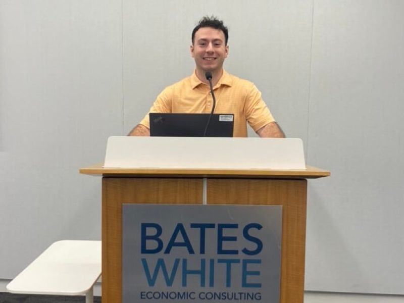 Byrne, Colin Colin Byrne, who will graduate from Penn State in 2025, stands behind a podium that reads Bates White Economic Consulting on the front.